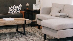 Un salon avec un canapé gris, un tapis à motifs, une table basse en bois et une petite table d’appoint sur laquelle se trouvent un globe terrestre et un symbole indiquant la présence d’une connexion Wi-Fi.