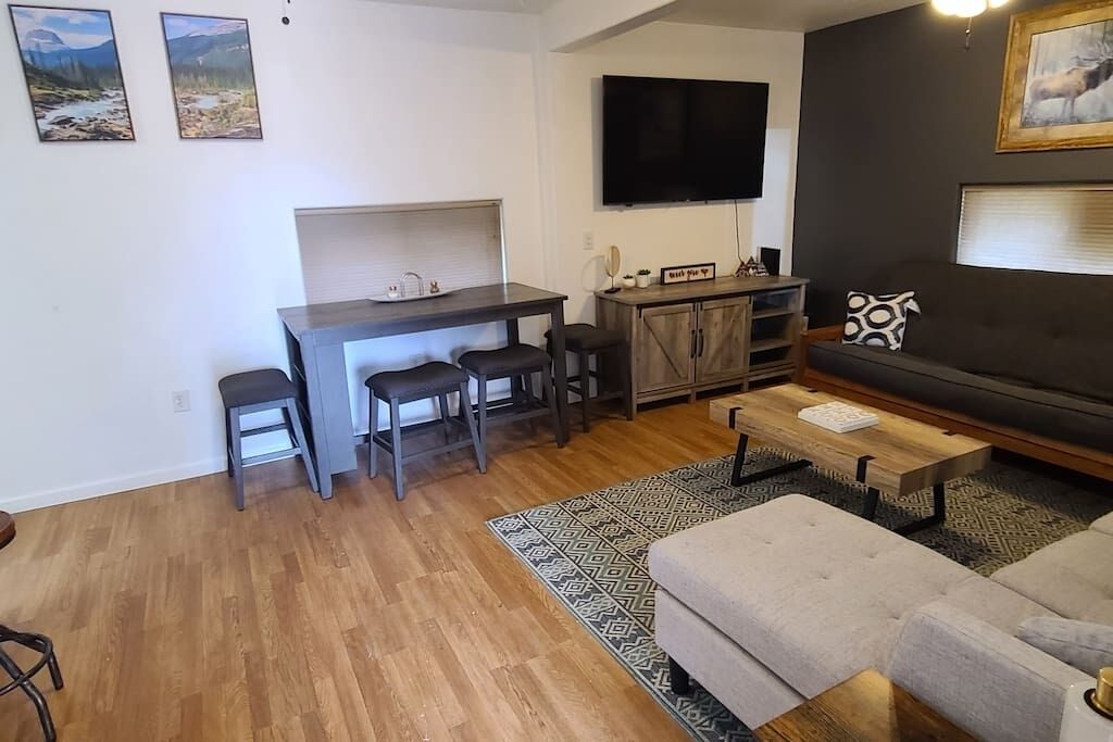 Ein modernes Wohnzimmer mit einer Couch, einem Couchtisch, einem an der Wand befestigten Fernseher und einer Küchenzeile mit einer Arbeitsplatte und Barhocker.