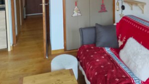 A room with a wooden ceiling, a bed with a red blanket, a small table, and a wardrobe.