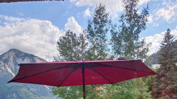 A balcony with wicker furniture and a red umbrella, overlooking a mountainous landscape.