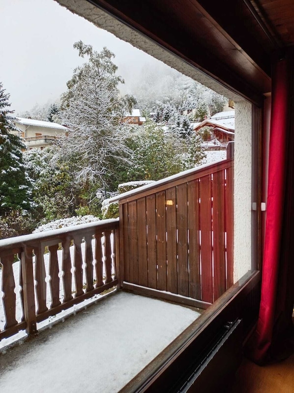 A balcony with a wooden railing and a view of a snowy landscape with houses and trees.
