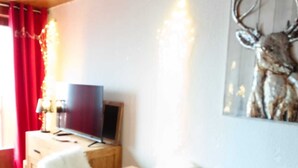 A dining area with a table and chairs, a television on a stand, and a deer artwork on the wall.
