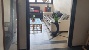 Un salon avec un canapé, une table basse et une petite table d’appoint sur laquelle est posée une plante. Il y a une fenêtre donnant sur l’extérieur.