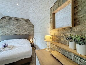 Un dormitorio con cama, mesita de noche, lámpara y plantas en macetas.