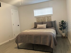 A bedroom with a bed, a window with blinds, a door, and a potted plant.