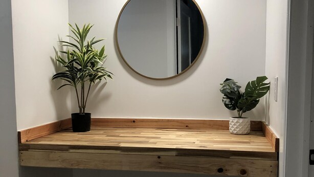 A small, enclosed room with a wooden bench, a round mirror, and two potted plants.