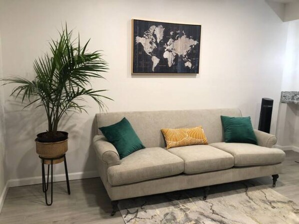 A living room with a beige sofa, a world map on the wall, a potted plant, and a patterned rug.