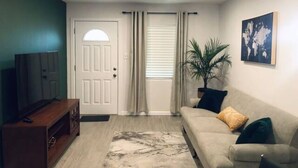 A living room with a sofa, a TV, a wooden cabinet, a plant, and a door with curtains.