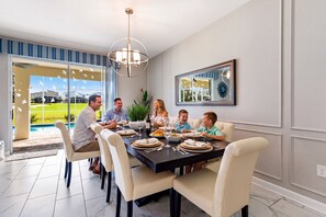 Un coin repas avec une table dressée pour un repas de famille, un lustre et une vue sur une piscine.