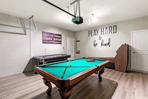 Uma mesa de bilhar em uma sala com uma placa que diz 'FEELS LIKE FUNSHINE GAME ROOM' e outra placa que diz 'PLAY HARD & be kind'.