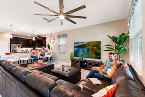 Uma sala de estar moderna com um sofá de couro preto, uma televisão e uma área de jantar ao fundo.