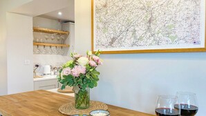 A wooden dining table with a glass vase of flowers, bowls of olives and cheese, and two glasses of red wine. - South Riccalton Farm Cottage (Jedburgh)