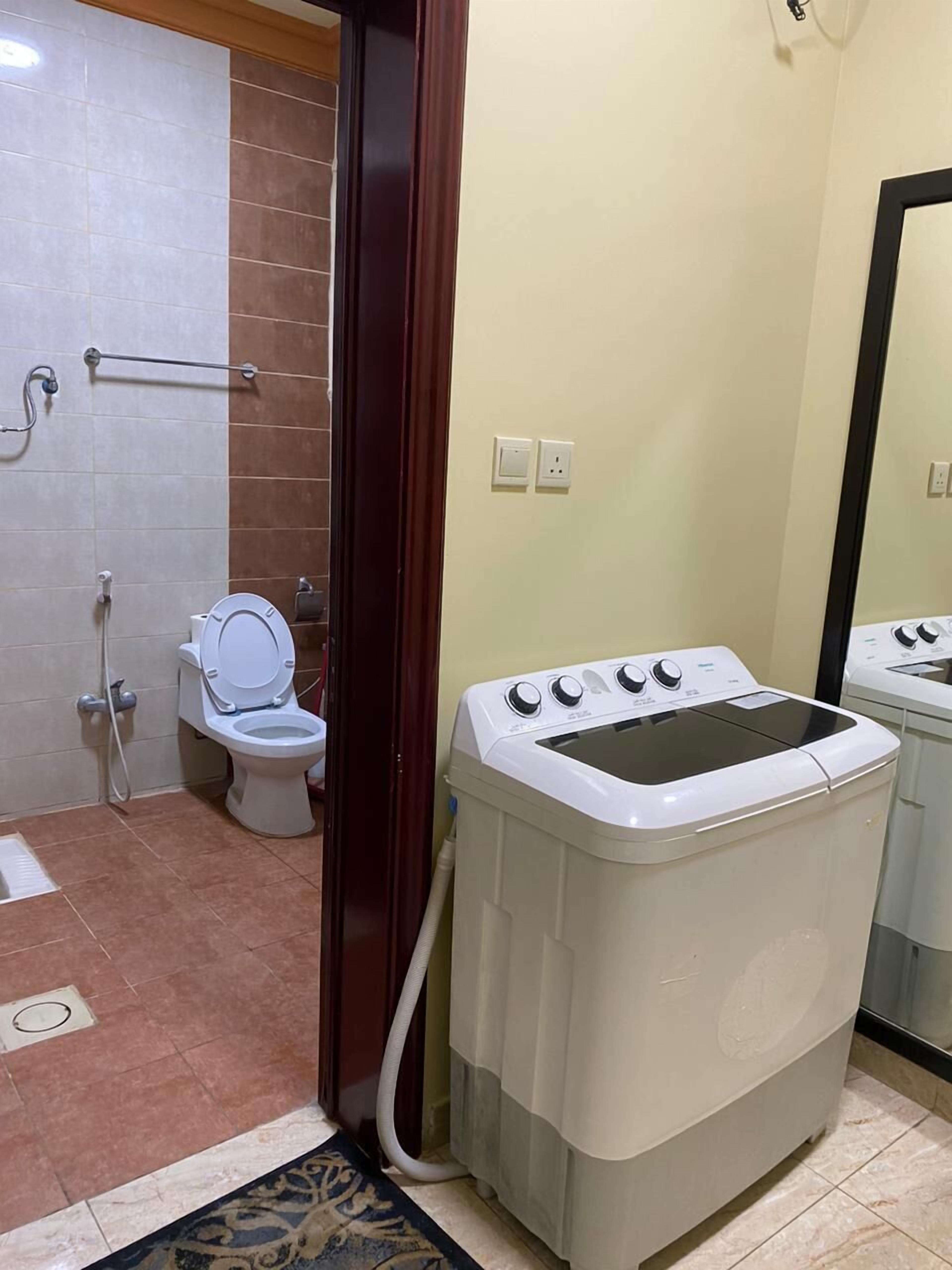 A compact bathroom with a toilet, a washing machine, and a shower.