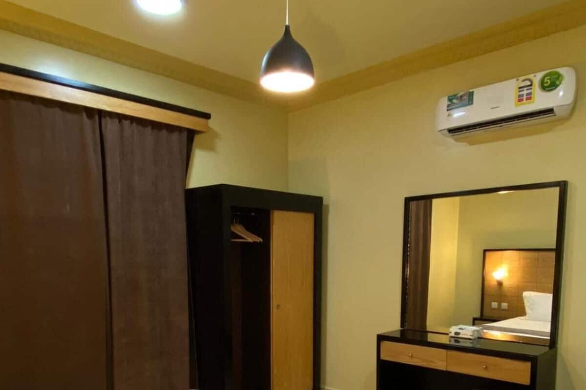 A hotel room with a bed, a desk, a wardrobe, a mirror, and an air conditioning unit.