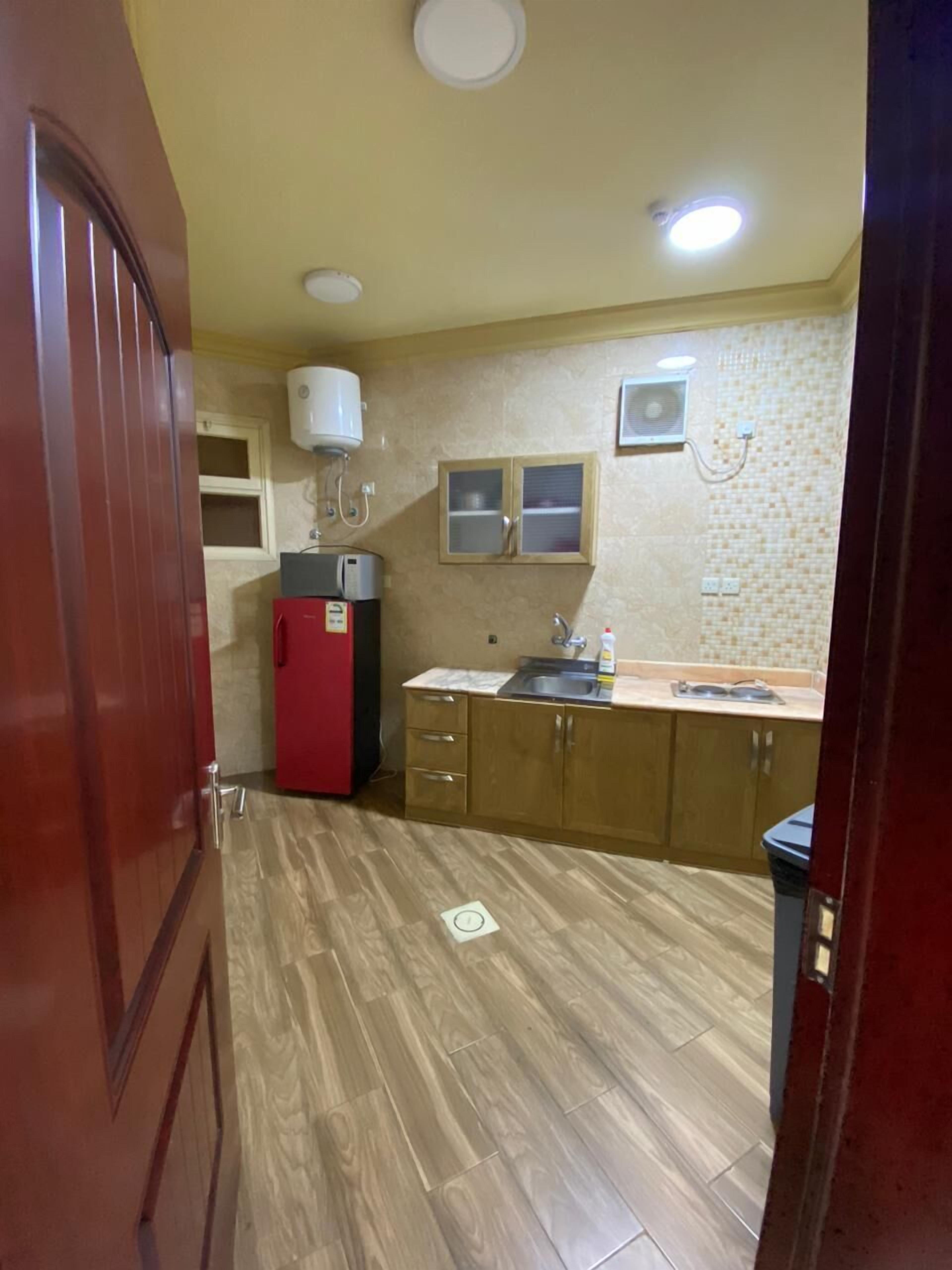 Eine kleine Küche mit Holzschränken, einem roten Kühlschrank, einer Spüle und einem Fenster darüber.