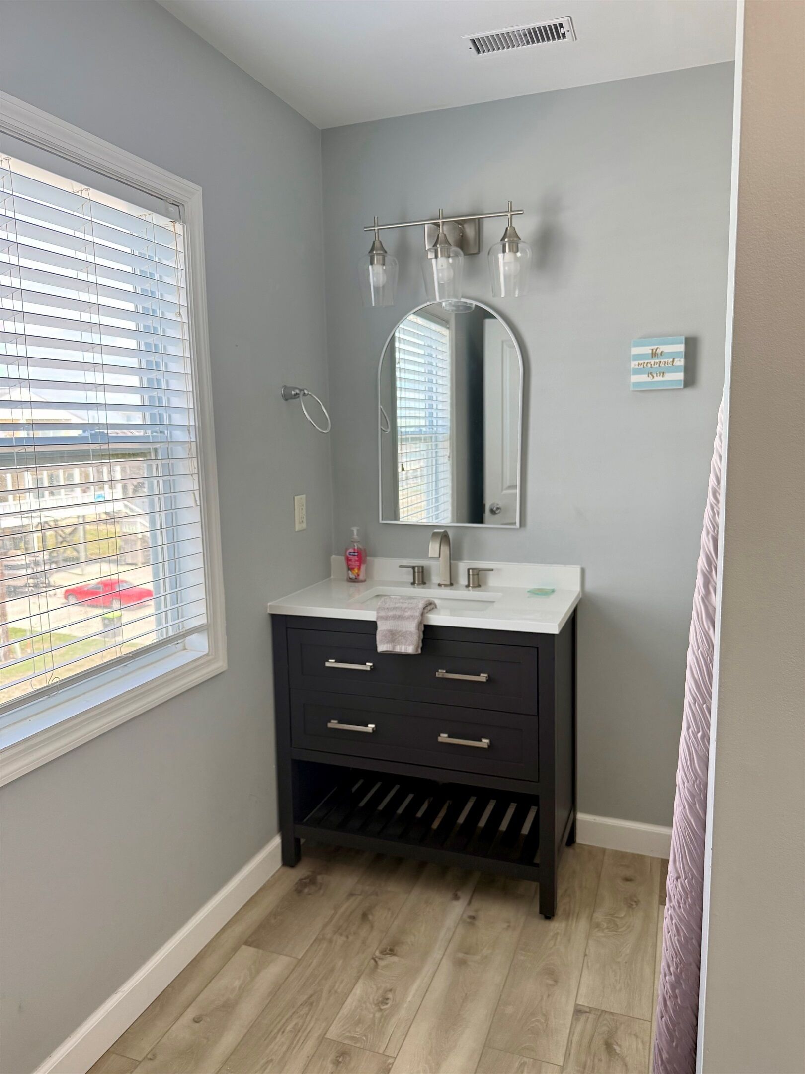 A bathroom with a window, a mirror, a sink, and a towel rack.