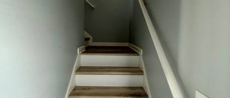 Una escalera de madera con barandillas blancas que lleva a un rellano con una lámpara fijada a la pared.