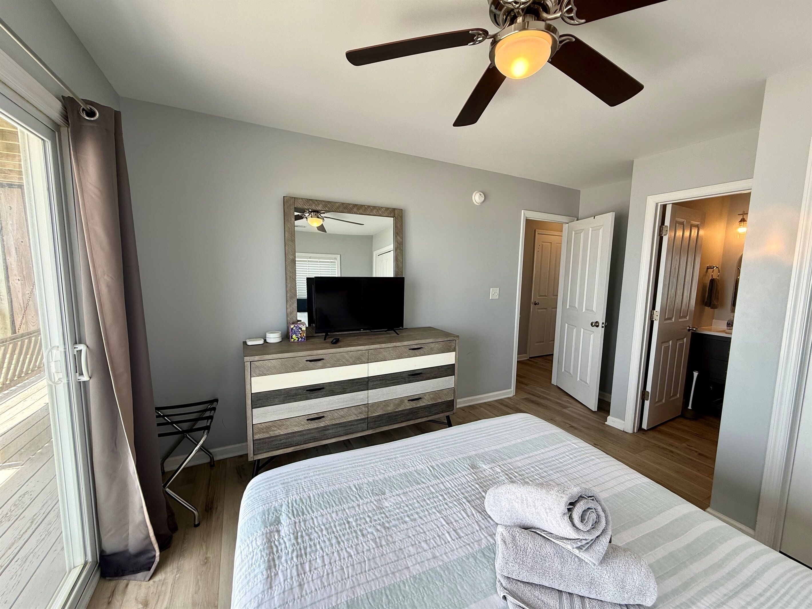 A bedroom with a bed, a dresser, a television, a ceiling fan, and a bathroom door.
