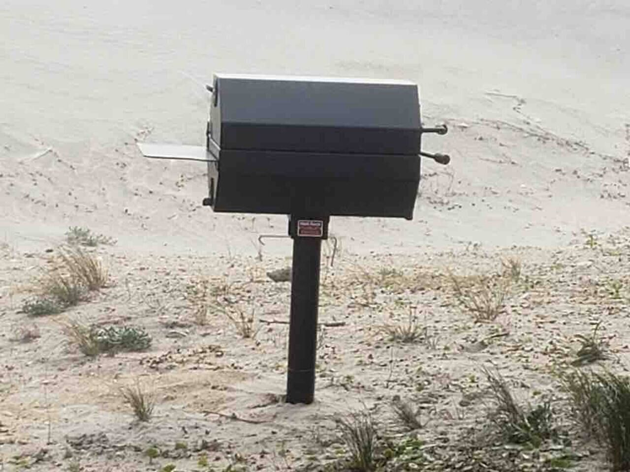 A black outdoor mailbox on a sandy surface with sparse vegetation.