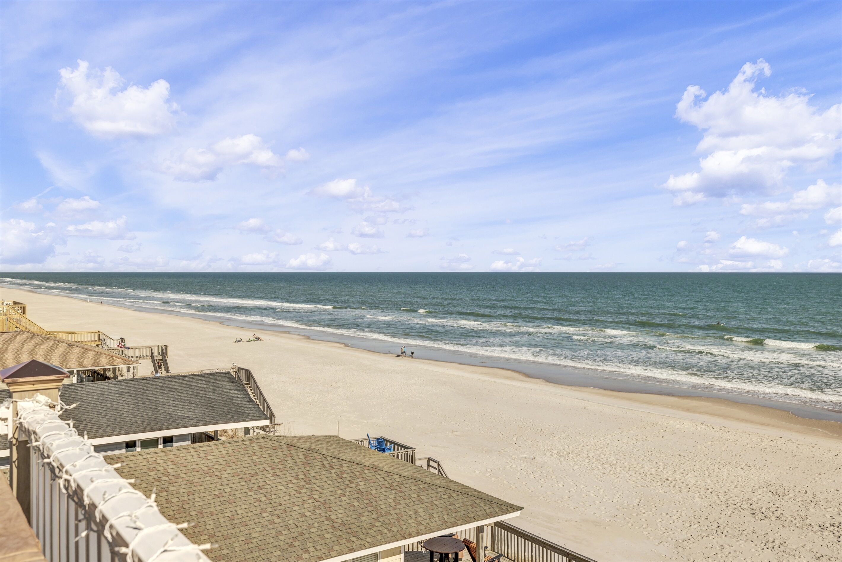 Une vue sur la plage avec un bâtiment au premier plan, une plage de sable et l’océan.