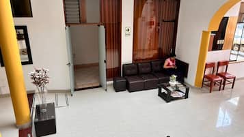 Un hall d’entrée spacieux comprenant un espace détente avec des sièges, un comptoir d’accueil et un chemin dégagé menant à une sortie.