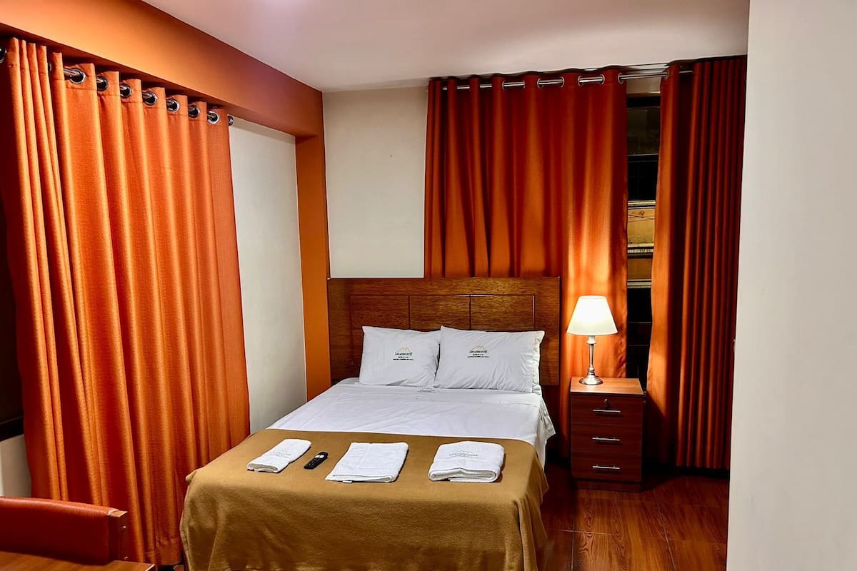 A hotel room with a bed, a nightstand, a lamp, and a wardrobe.