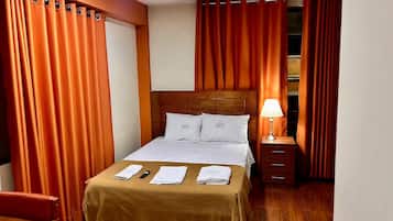Una habitació d'hotel amb un llit, una tauleta de nit, una làmpada i un armari.