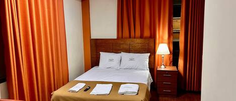 Una habitación de hotel con una cama, una mesita de noche, una lámpara y un armario.