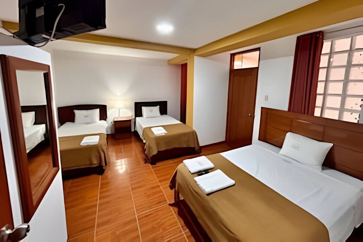 A hotel room with three single beds and one double bed, wooden flooring, and a large window with curtains.