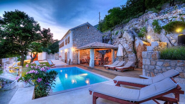 Ein Steinhaus mit Pool, Sitzgelegenheit im Freien und einer Steinmauer.