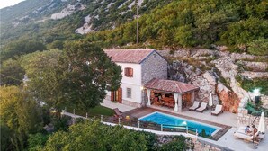 Eine Villa mit Pool, Steinmauern und Blick auf die umliegenden Berge.