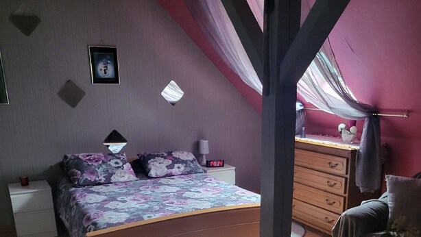 Ein Schlafzimmer mit einem Bett, einem Nachttisch, einer Kommode, einem kleinen Tisch und einem Fenster mit Vorhängen.