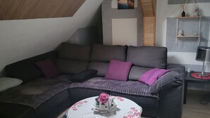 Ein modernes Wohnzimmer im Loft-Stil mit einer Eckcouch, einem runden Couchtisch mit floraler Dekoration und einem Oberlicht.