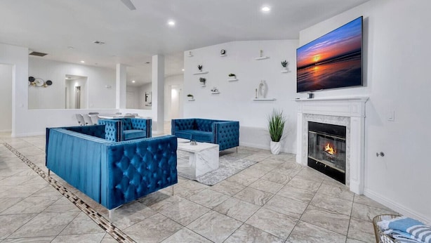 Un salon moderne avec une cheminée, des canapés bleus recouverts de tissu, une table basse blanche et un grand téléviseur fixé au mur.