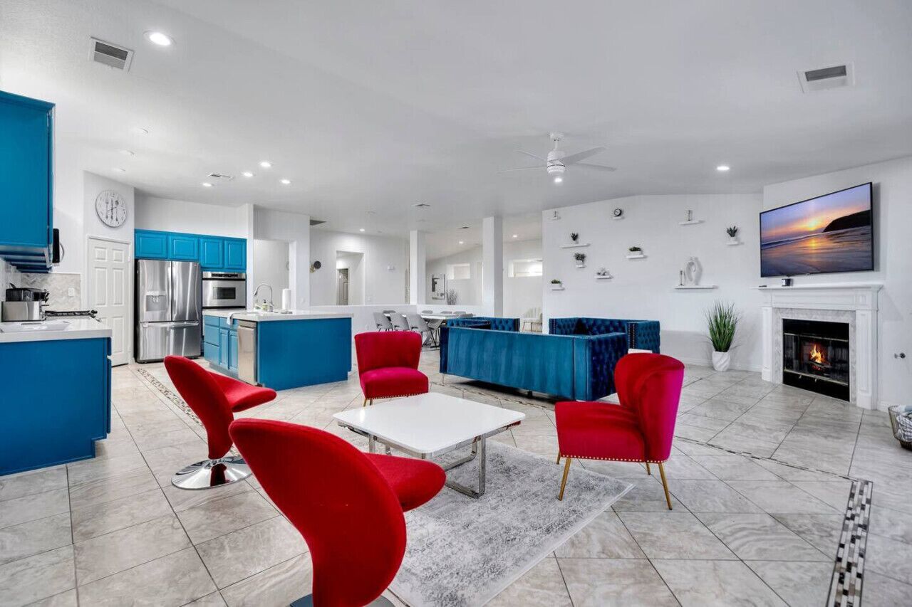 A modern kitchen with blue cabinets, a dining area with red chairs, a fireplace, and a TV mounted on the wall.