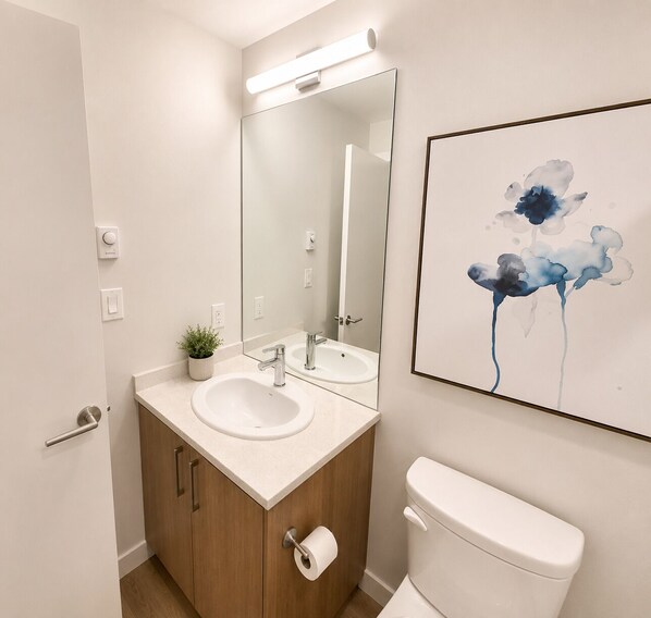 Un baño moderno con lavamanos doble, armarios de madera, inodoro, espejo y lámpara empotrada en la pared.