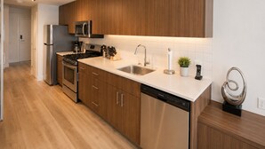 A modern kitchen with wooden cabinets, stainless steel appliances, and a dishwasher. - Perfect Studio Downtown Sidney (Victoria)