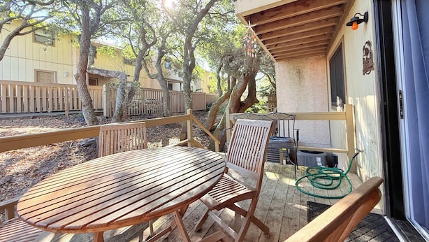Eine Holzterrasse mit Tisch und Stühlen, umgeben von Bäumen und einem Gebäude mit einem Balkon.