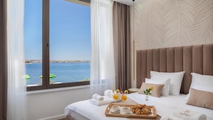 A hotel room with a large window overlooking a body of water, a bed with white linens, a wooden tray with croissants and juice, and a vase with a single flower. - Awesome home in Tkon-Ugrinic (Tkon-Ugrinic)