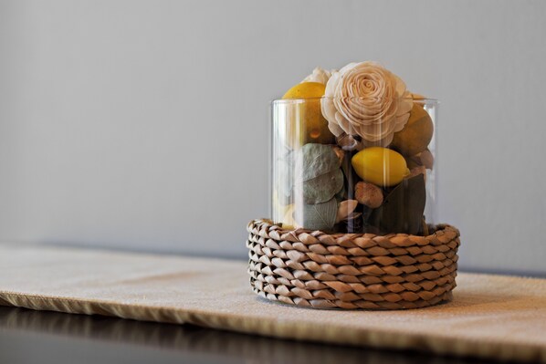A clear glass container with a woven basket base, containing rocks, a yellow flower, and a white flower.