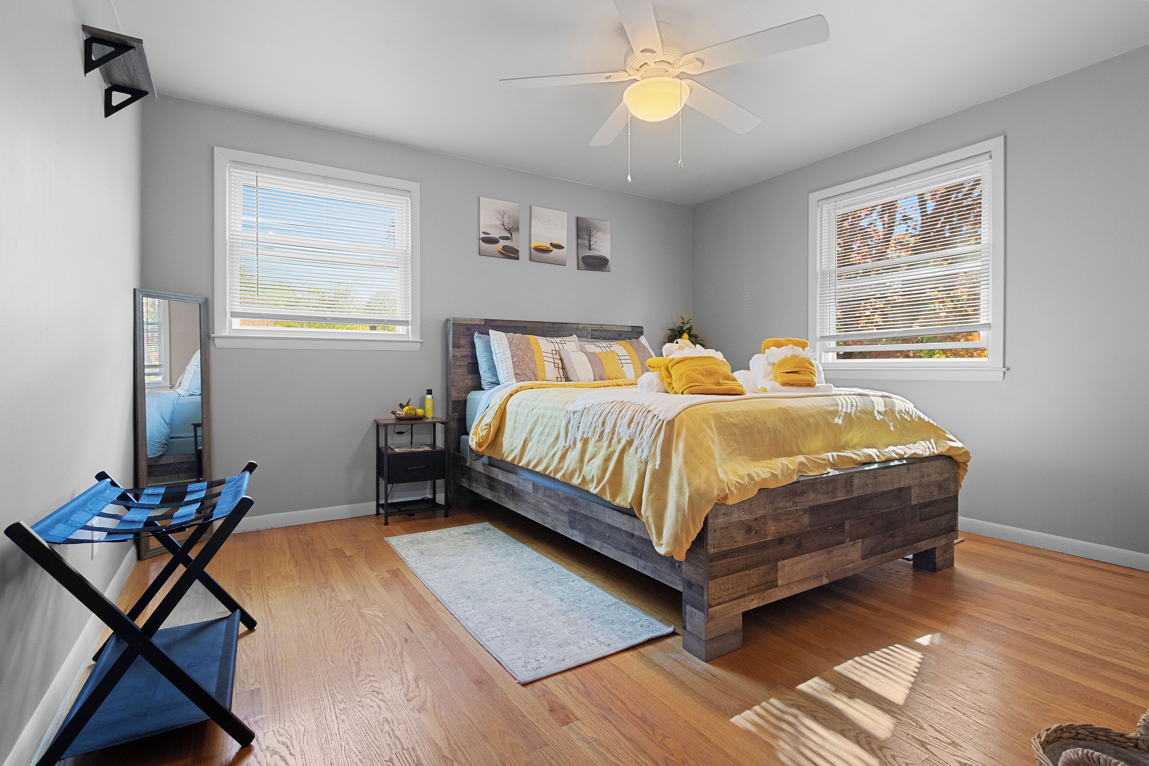 A bedroom with a bed, a ceiling fan, and two windows with blinds.