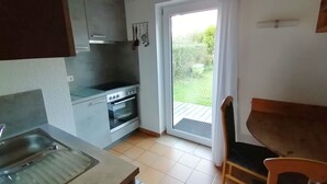 Une cuisine compacte dotée d’un four encastré, d’une plaque de cuisson et d’un petit coin repas avec une table et une chaise.