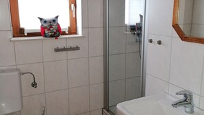 Une salle de bain avec des toilettes, un lavabo et une douche. Il y a une fenêtre donnant sur l’extérieur.