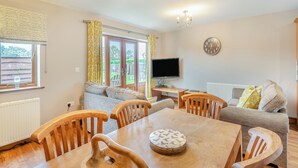 A dining area with a wooden table and chairs, a television, and a sofa. - Lake View 2 - UK45578 (Louth)