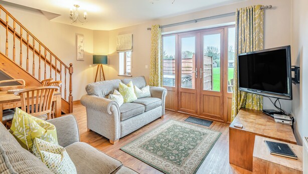 A spacious living room with a grey sofa, wooden chairs, a wooden desk, a television, and a staircase. - Lake View 2 - UK45578 (Louth)