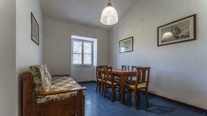 Una habitación con sofá de madera, una mesa de comedor con sillas, un ventanal y cuadros en las paredes.