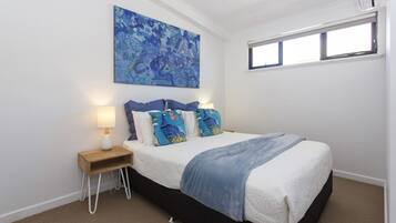 A bedroom with a bed, a nightstand, a lamp, a window, and a wall-mounted painting.