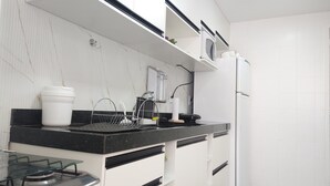 A modern kitchen with white cabinets, a black countertop, a gas stove, and a refrigerator. - Prainha PÉ NA Praia (Prainha Arraial do Cabo)