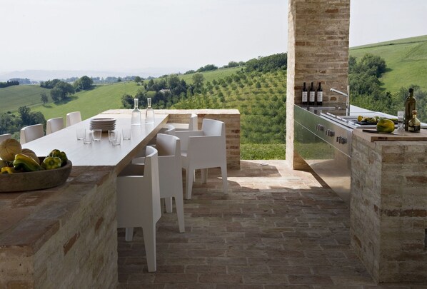 Ein Essbereich im Freien mit einem Steintisch und Stühlen, mit Blick auf einen Weinberg.