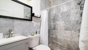 Un baño con pared de ducha de mármol, un inodoro y un lavabo.